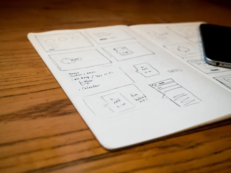 Hand-drawn app wireframes in a notebook next to a phone